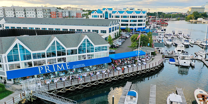 View of buildings and marina at 78 Southfield from Stamford Harbor, including outdoor diners at Prime restaurant